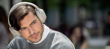    A male in the street wearing the Sony WH-1000XM3 Headphones enjoying music, with background street and people blurred